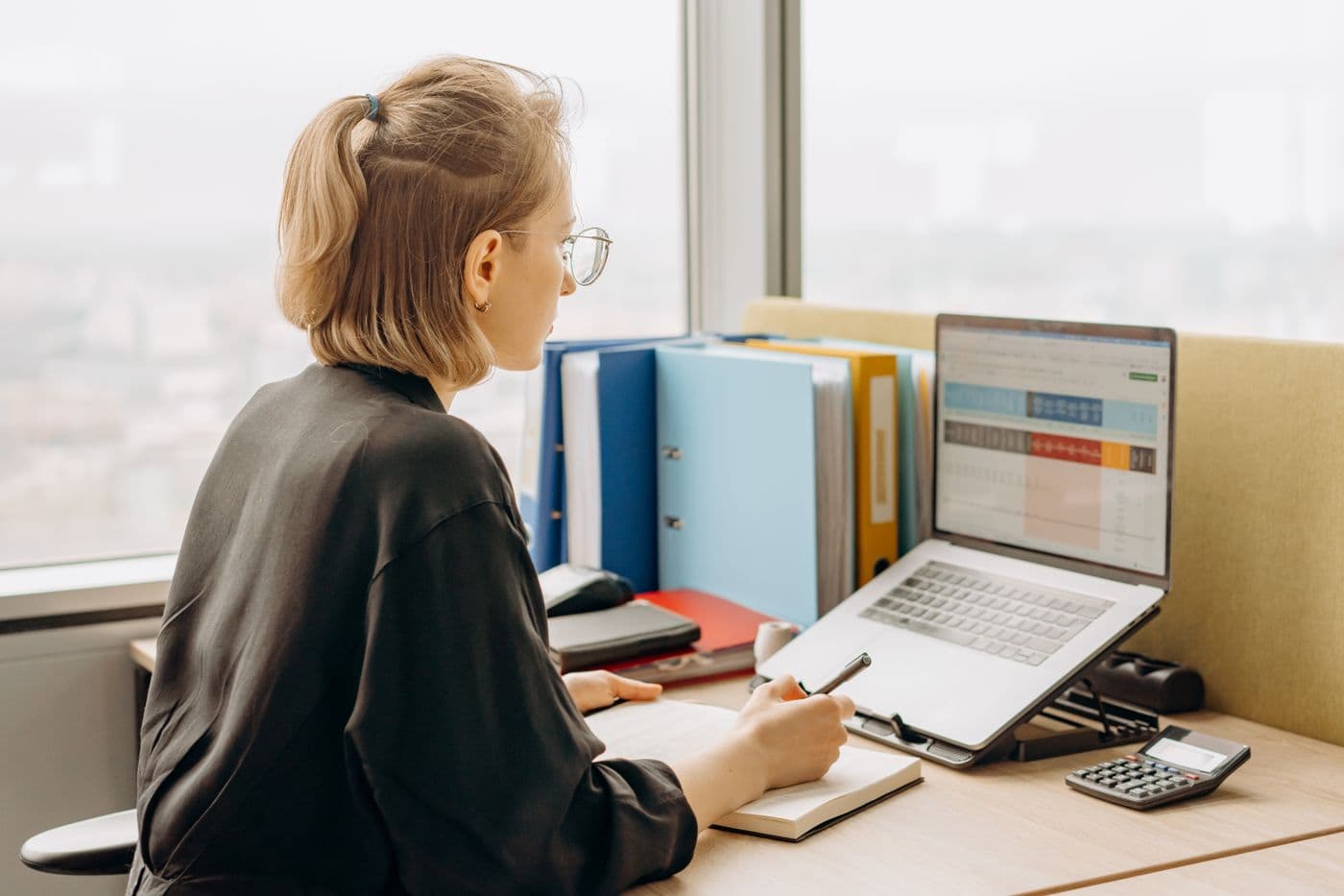 A specialist reviewing and organizing a business's listing data in a spreadsheet beside color-coded files