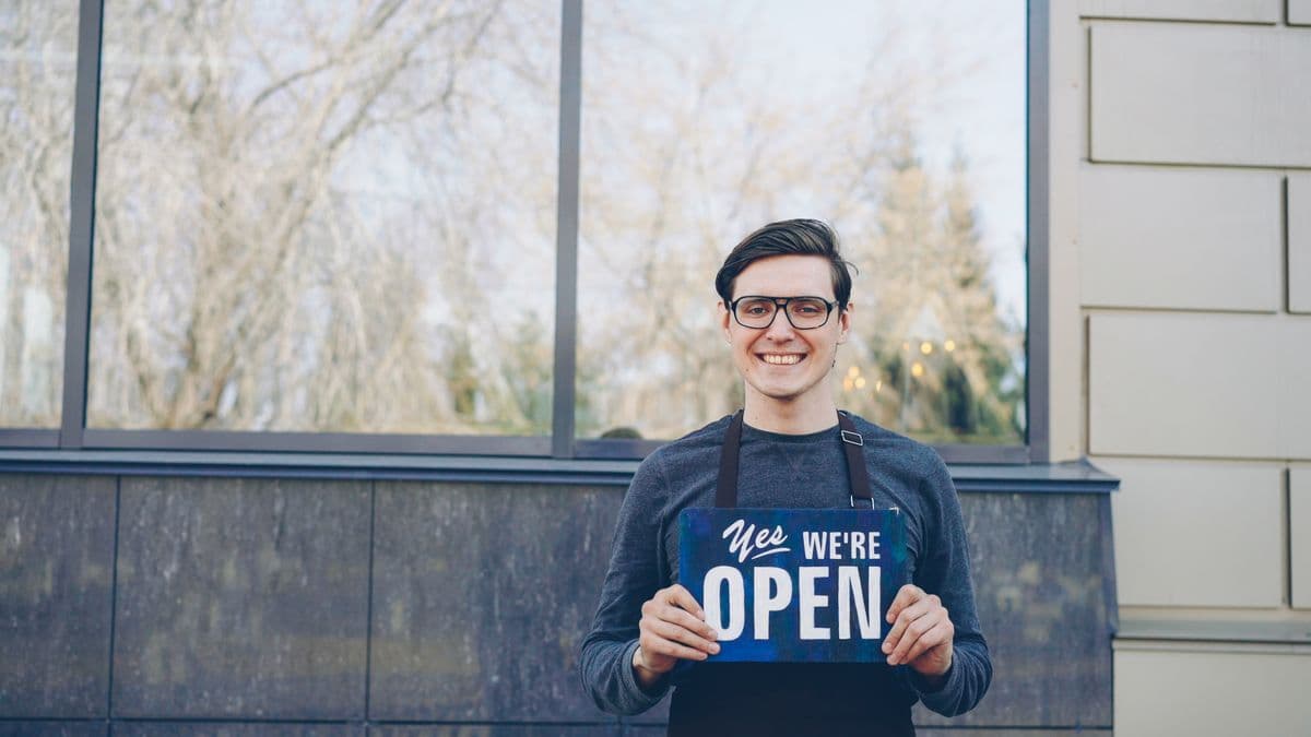 A smiling local business owner holding a we're open sign outside their shop